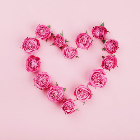 Floral heart made of pink rose flowers on pastel background top view. Flat lay styling. Fashion and creative composition.の写真素材