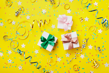 Gift or present box decorated colorful confetti, star, candy and streamer on yellow table top view. Flat lay style. Birthday background.の写真素材