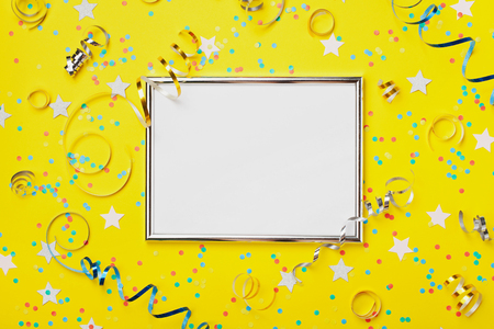 Party, carnival or birthday background decorated silver frame with colorful confetti and streamer on yellow table top view. Flat lay style. Holiday mockup. Greeting card with copy space.の写真素材