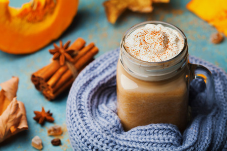 Warm pumpkin spiced latte or coffee in cup decorated knitted scarf on turquoise vintage background. Autumn, fall or winter hot drink. Cozy breakfast.の写真素材