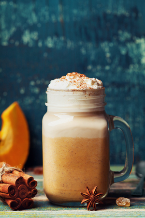 Hot pumpkin spiced latte or coffee in cup decorated cinnamon on teal vintage table. Autumn, fall or winter beverage. Cozy breakfast.の写真素材