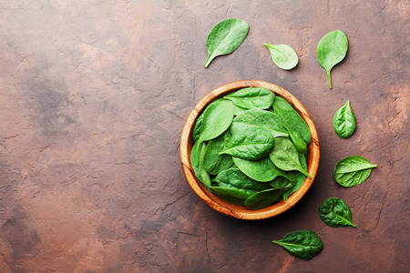 Organic food. Baby spinach leaves in wooden bowl on rustic stone table top view. Copy space for text.の写真素材