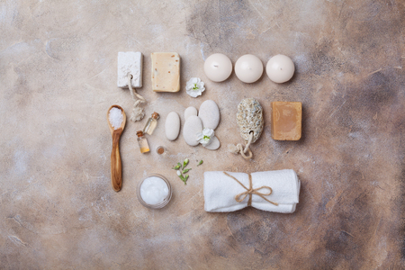 Spa and beauty setting from handmade soap, bath scrub, candles, oil and towel decorated flowers on stone background top view. Flat lay.の写真素材