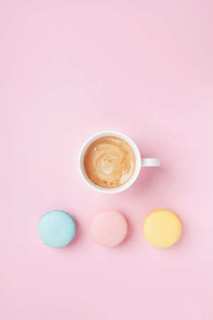 Cake macaron and cup of coffee on pastel pink background top view. Cozy morning breakfast. Fashion flat lay.の写真素材