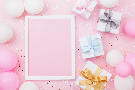Birthday or holiday mockup with frame, gift box, pastel balloons and confetti on pink table top view. Flat lay composition.の写真素材