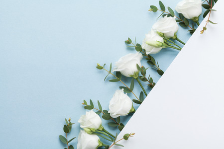 Wedding mockup of paper card decorated beautiful white flowers and green leaves on pastel background top view. Flat lay style.の写真素材