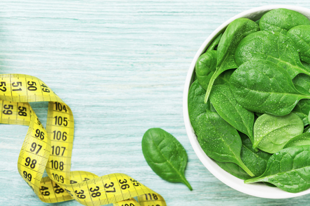 Tape measure and spinach leaves in bowl top view. Diet and healthy food concept.の写真素材