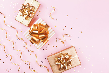 Fashion gift or present boxes with golden bows, serpentine and star confetti on pink pastel table top view. Flat lay composition for birthday, christmas or wedding.の写真素材