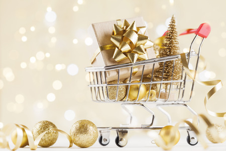 Shopping cart with gift or present box on golden bokeh background. Christmas and New year sale concept.の写真素材