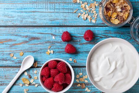 Healthy breakfast with greek yogurt, raspberries and muesli on blue wooden table top view.の写真素材