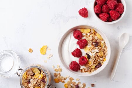 Greek yogurt in bowl with raspberries and muesli on white table top view. Healthy  breakfast.の写真素材