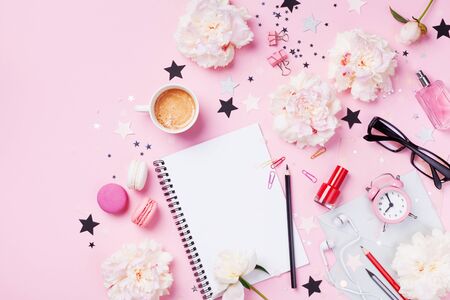 Coffee, macaroons, alarm clock, office supply, peony flowers and notebook on pink pastel table top view. Flat lay style. Beautiful morning breakfast. Fashion woman working desk.の写真素材