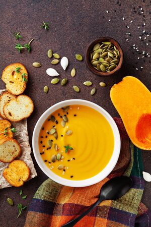 Bowl with diet autumn pumpkin cream soup served with seeds and crouton on stone table top view.の写真素材