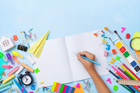 School supplies and stationery with children hand writing in empty notebook top view. Education,...