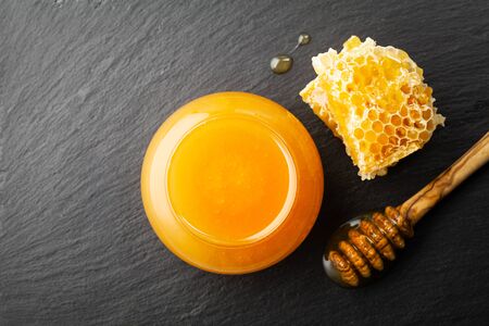 Honey in jar, dipper and honeycomb on black table top view.の写真素材