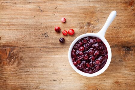 Cranberry sauce in ceramic saucepan with berries on wooden table top view.の写真素材
