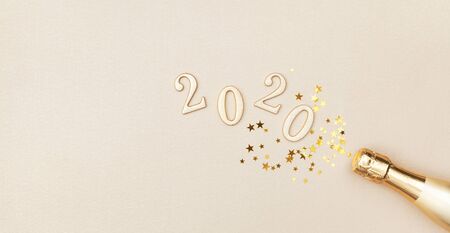 Creative Christmas and New Year greeting card with golden champagne bottle, confetti stars and 2020 numbers. Flat lay. Banner format.の写真素材