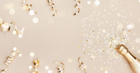 Champagne bottle with confetti stars, bokeh decoration and party streamers on golden background. Christmas, birthday or wedding concept. Flat lay.の写真素材