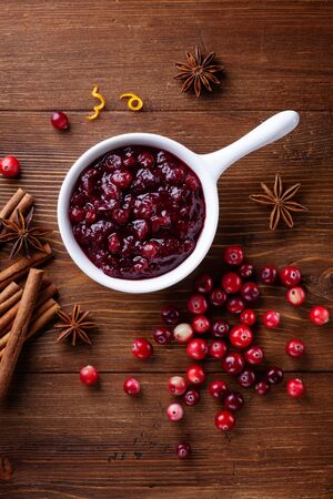Cranberry sauce in ceramic saucepan with ingredients for cooking on kitchen wooden table from above.の写真素材