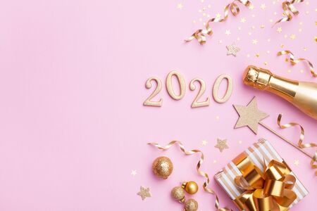Champagne bottle, golden gift or present box, 2020 number and confetti on pink background top view. Christmas and New Year greeting card. Flat lay.の写真素材