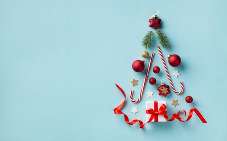 Creative Christmas fir tree made of gift box and holiday decorations on blue background top view. New Year greeting card. Flat lay.の写真素材