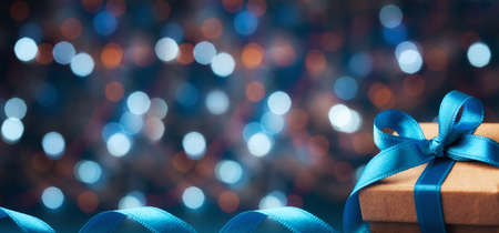 Christmas gift box or present with bow ribbon on magic blue bokeh background. Banner format.の写真素材