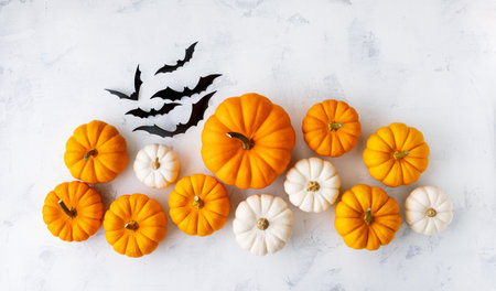 Halloween holiday card with party decorations of pumpkins and bats on white stone table top view. Happy halloween greeting poster in flat lay style.の写真素材