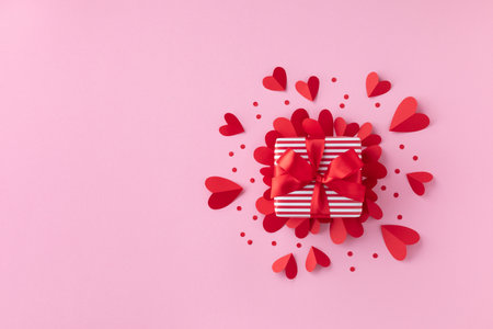 Gift or present box and paper hearts on pink table for Valentine day greeting card. Flat lay style.の写真素材