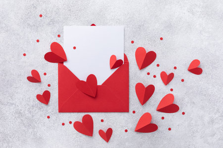 Valentine day background with envelope, paper card and various red hearts on white table for love...