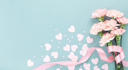 Happy mothers day composition. Pink carnation flowers and paper hearts on pastel blue background top view.の写真素材