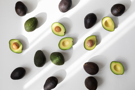 Heap of ripe whole and half avocados on white background top view in aesthetic shadow sunlight. Flat lay style.の写真素材