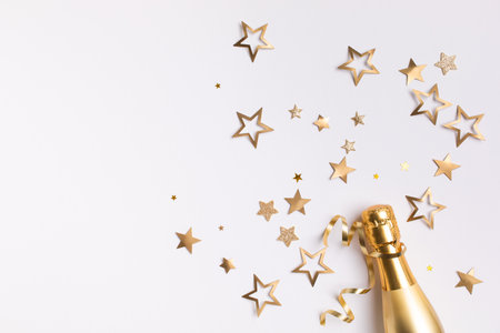 Champagne bottle with confetti stars and party streamers on white festive background. Christmas, birthday or wedding concept. Flat lay.の写真素材