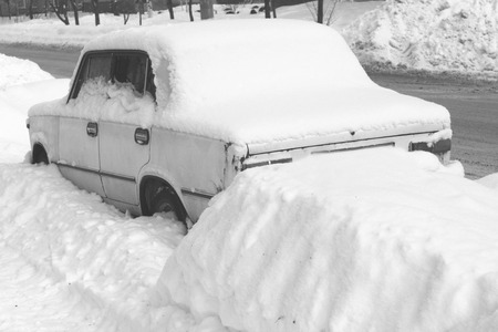 Old car in winter in snow on road, black and white photoの写真素材