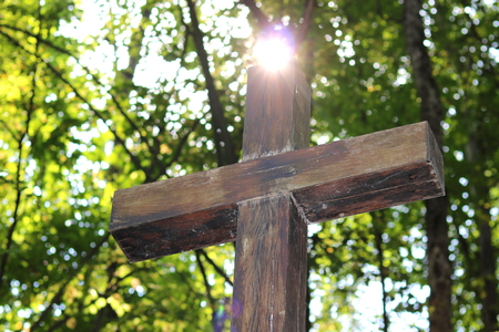 Wooden Christian cross on the background of green trees and rays of sunlight at dawnの写真素材