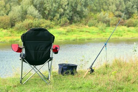 Fishing chair, rod and bait on the river bank in autumnの写真素材