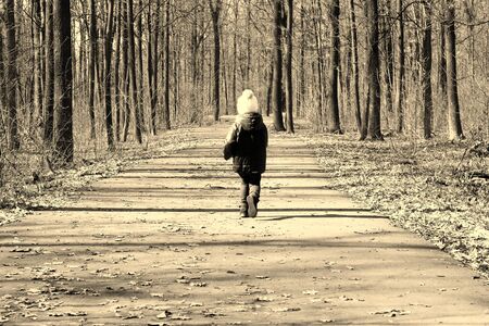 Little child runs along forest road between treesの写真素材