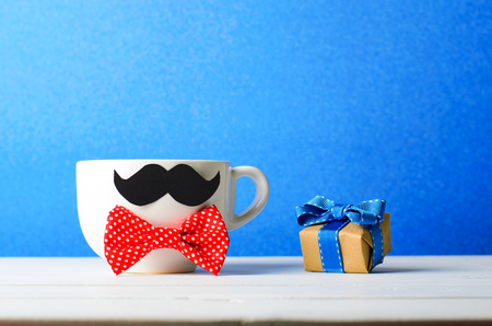 Coffee Mug with Mustache and Gift Box over Blue Background, Happy Father's Day Conceptの写真素材