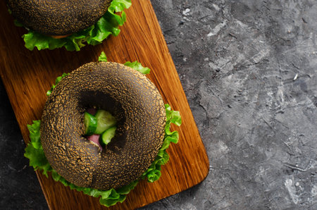Black Bagels Sandwiches with Cucumbers, Salad and Ham on Wooden Board and Dark Background, Tasty Snack or Breakfastの写真素材