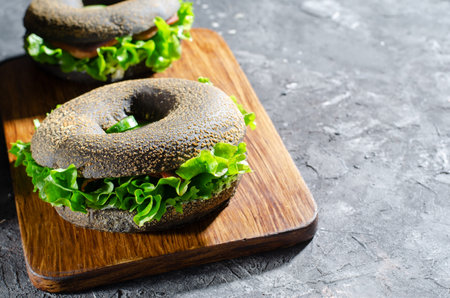 Black Bagels Sandwiches with Cucumbers, Salad and Ham on Wooden Board and Dark Background, Tasty Snack or Breakfastの写真素材