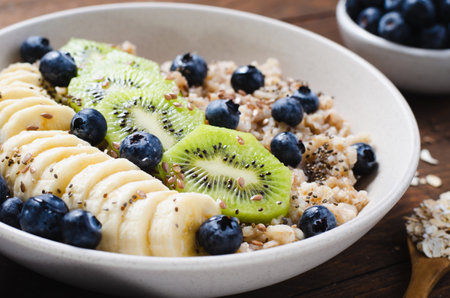 Oatmeal Bowl, Oat Porridge with Blueberry, Banana and Kiwi on Dark Rustic Background, Healthy Snack or Breakfastの写真素材