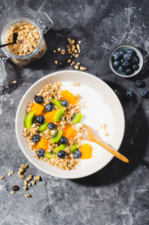 Yogurt with Granola, Kiwi, Blueberries, and Orange in a Bowl, Healthy Snack or Breakfast on Dark Backgroundの写真素材