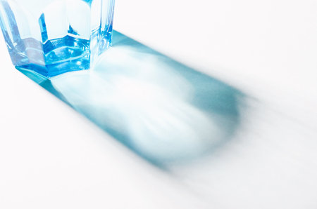 A Glass with Water and Sharp Shadows, Caustic Effect as Light Passes Through on Bright Backgroundの写真素材