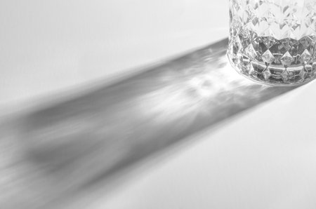 A Glass with Water and Sharp Shadows, Caustic Effect as Light Passes Through on Bright Backgroundの写真素材