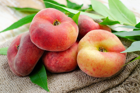 Fresh Flat Peaches, Chinese Saturn Donut Peaches with Leaves on Bright Backgroundの写真素材