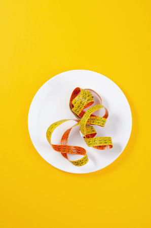 Diet, Weight Loss Concept, Empty Plate with Measuring Tape Over Yellow Background