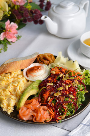 Healthy Breakfast with Salmon, Scrambled Eggs, Avocado, Vegetable Salad and Toppings on Bright Backgroundの写真素材