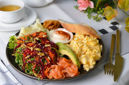 Healthy Breakfast with Salmon, Scrambled Eggs, Avocado, Vegetable Salad and Toppings on Bright Backgroundの写真素材