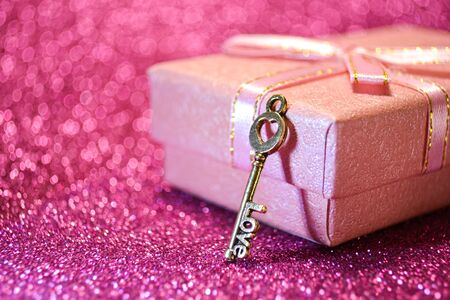 Little pink gift box with ribbon bow and golden love key on abstract glitter bokeh lights background. Holiday greeting card or banner. 14 february concept. Romantic Valentines day macro compositionの写真素材