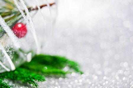 New Year holiday winter macro shot. Christmas tree and decor on silver glitter bokeh background. Transparent ball, white shine texture snow stripes, green branch, red berry. Banner with copy spaceの写真素材