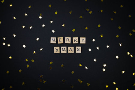 Holiday flat lay concept with merry christmas wooden letter word on black background. Gold yellow...